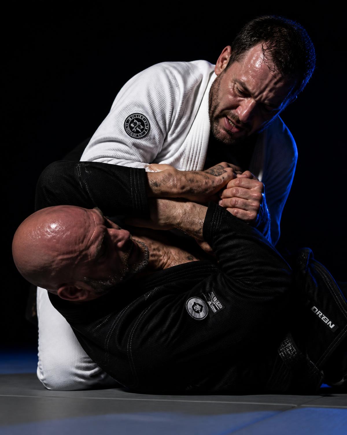 Praticantes adultos de Jiu-Jitsu de kimono durante um rola no tatame